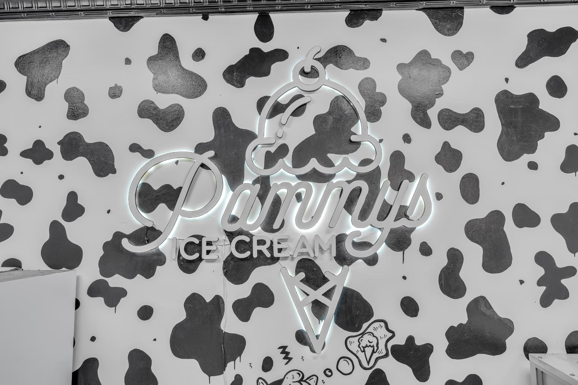 The illuminated Pammy's Ice Cream sign on a hand-painted cow-spot wall