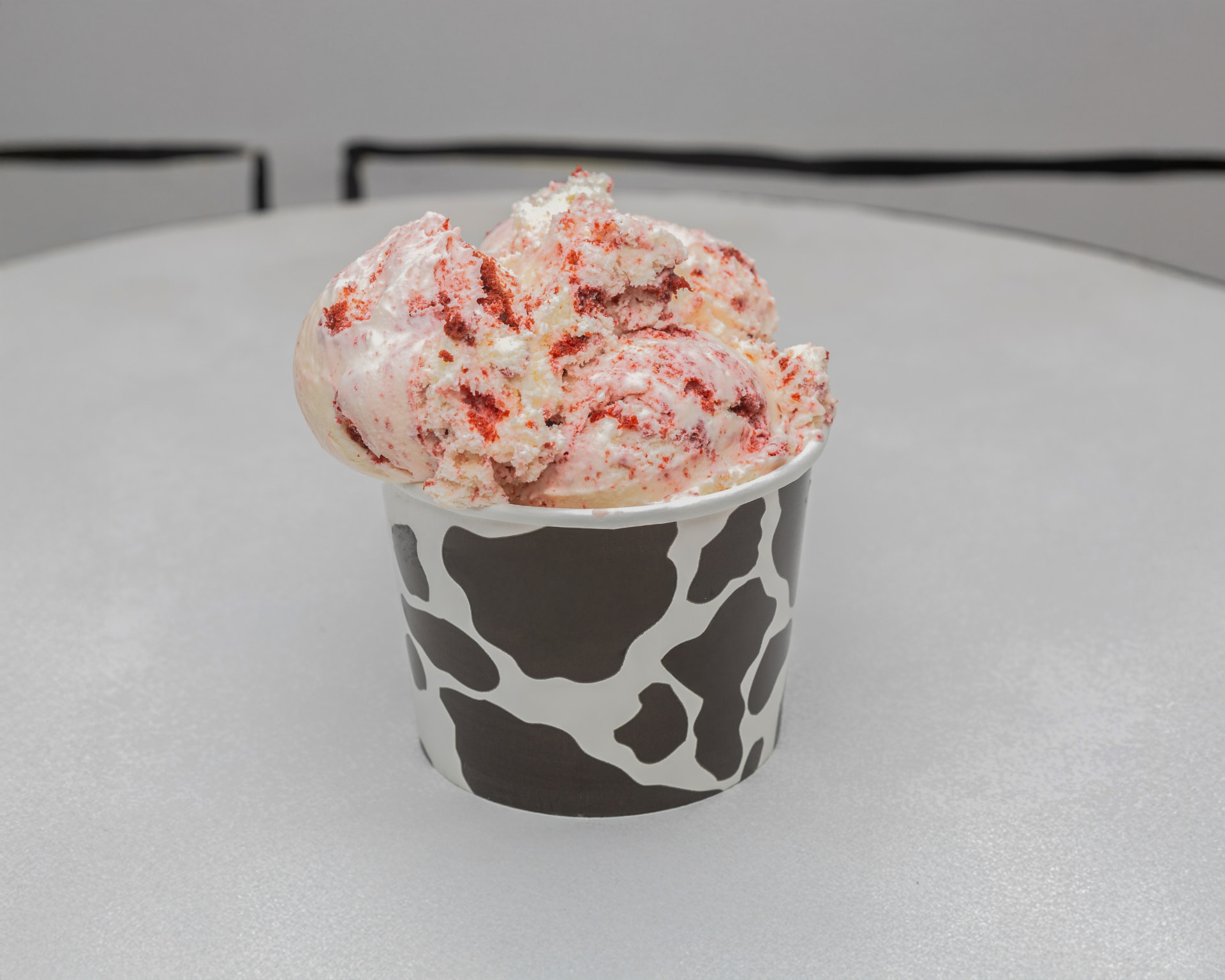 Triple scoop of red velvet ice cream with cake pieces in a cow-print cup