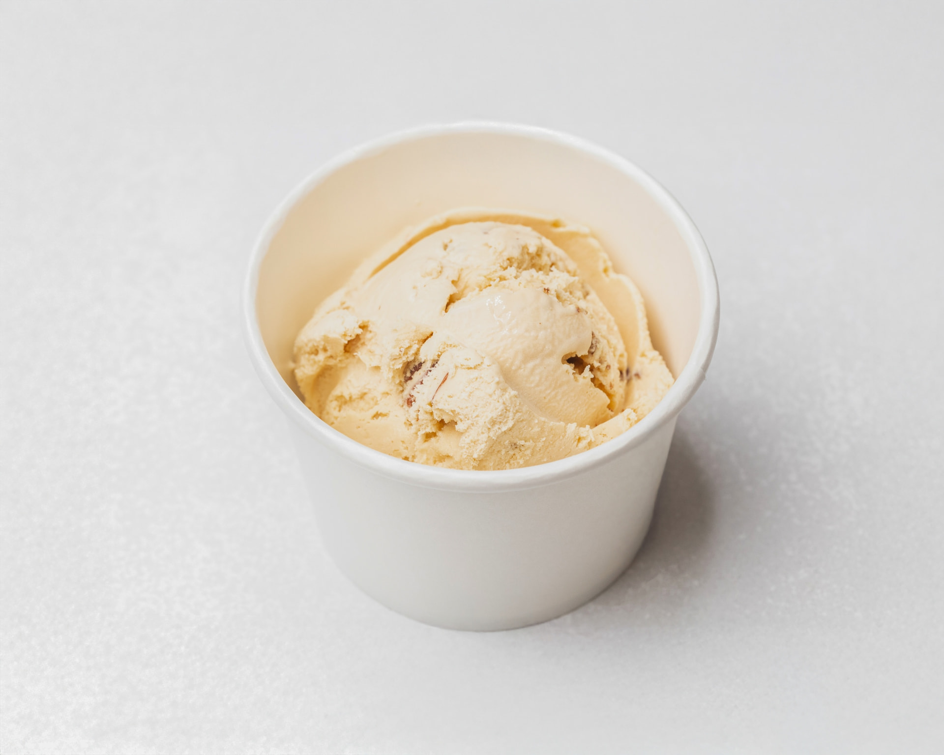 Butter pecan ice cream with pecan pieces in a white cup