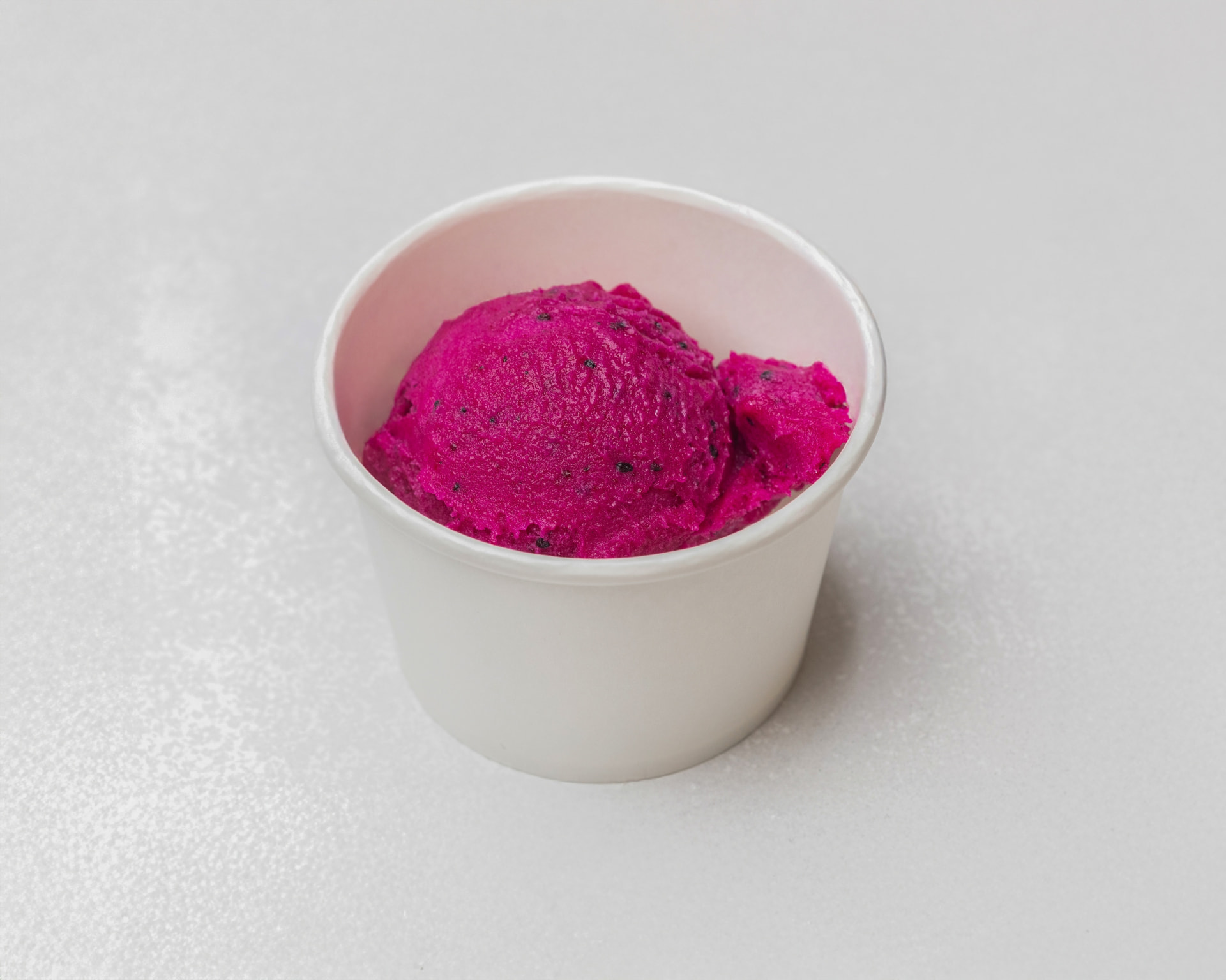 Bright magenta dragon fruit ice cream in a white cup