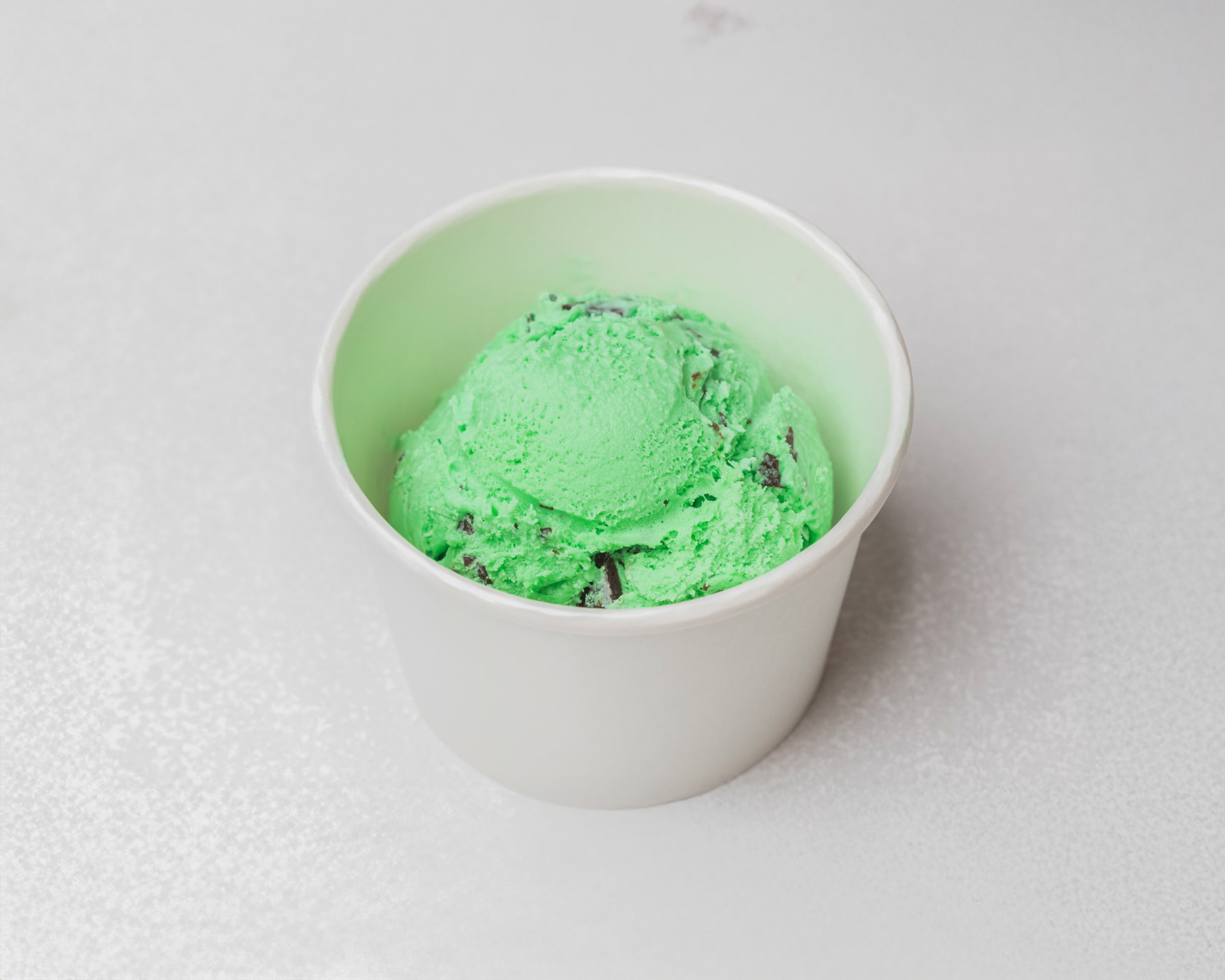Green mint chocolate chip ice cream in a white cup